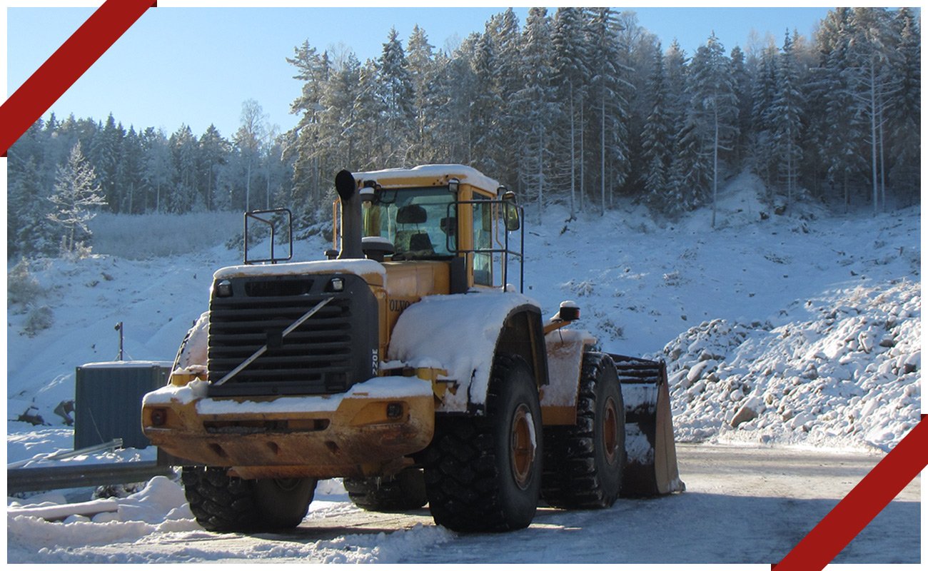 En Volvo-hjullæsser står parkeret foran en snedækket skov.
