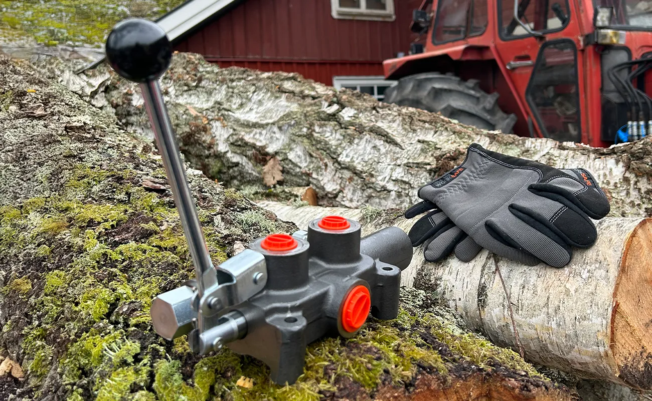 En monoblockventil f&ouml;r vedklyv &auml;r placerad p&aring; ett nedhugget tr&auml;d. Bakom ligger ett par arbetshandskar.