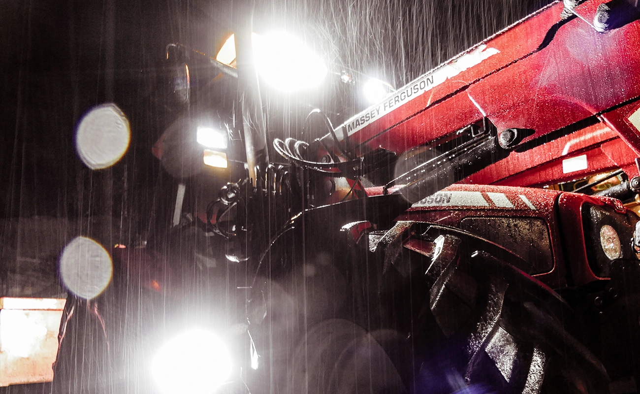 En Massey Ferguson-traktor med lykter som lyser opp regnet.