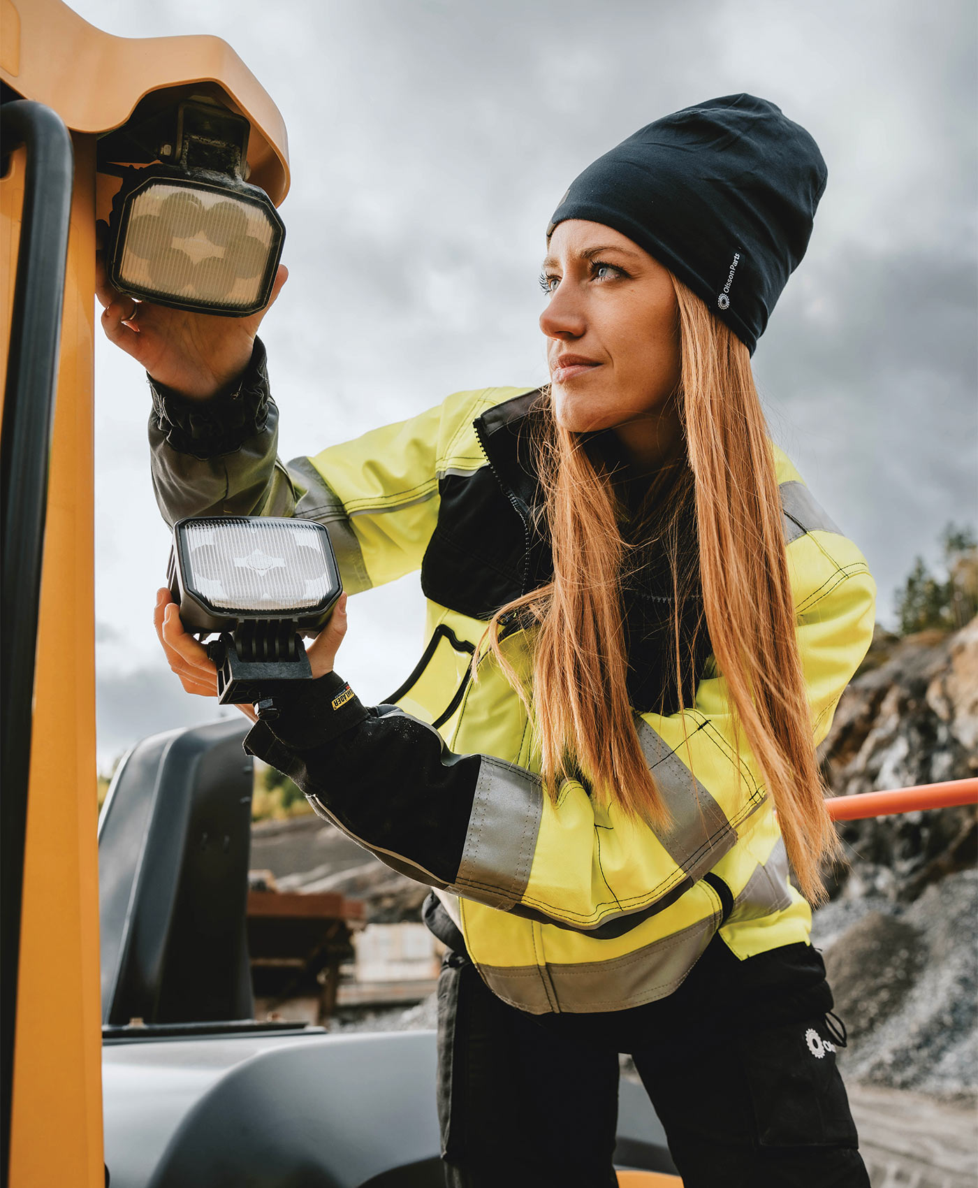A person is installing vehicle lighting on a yellow construction machine.