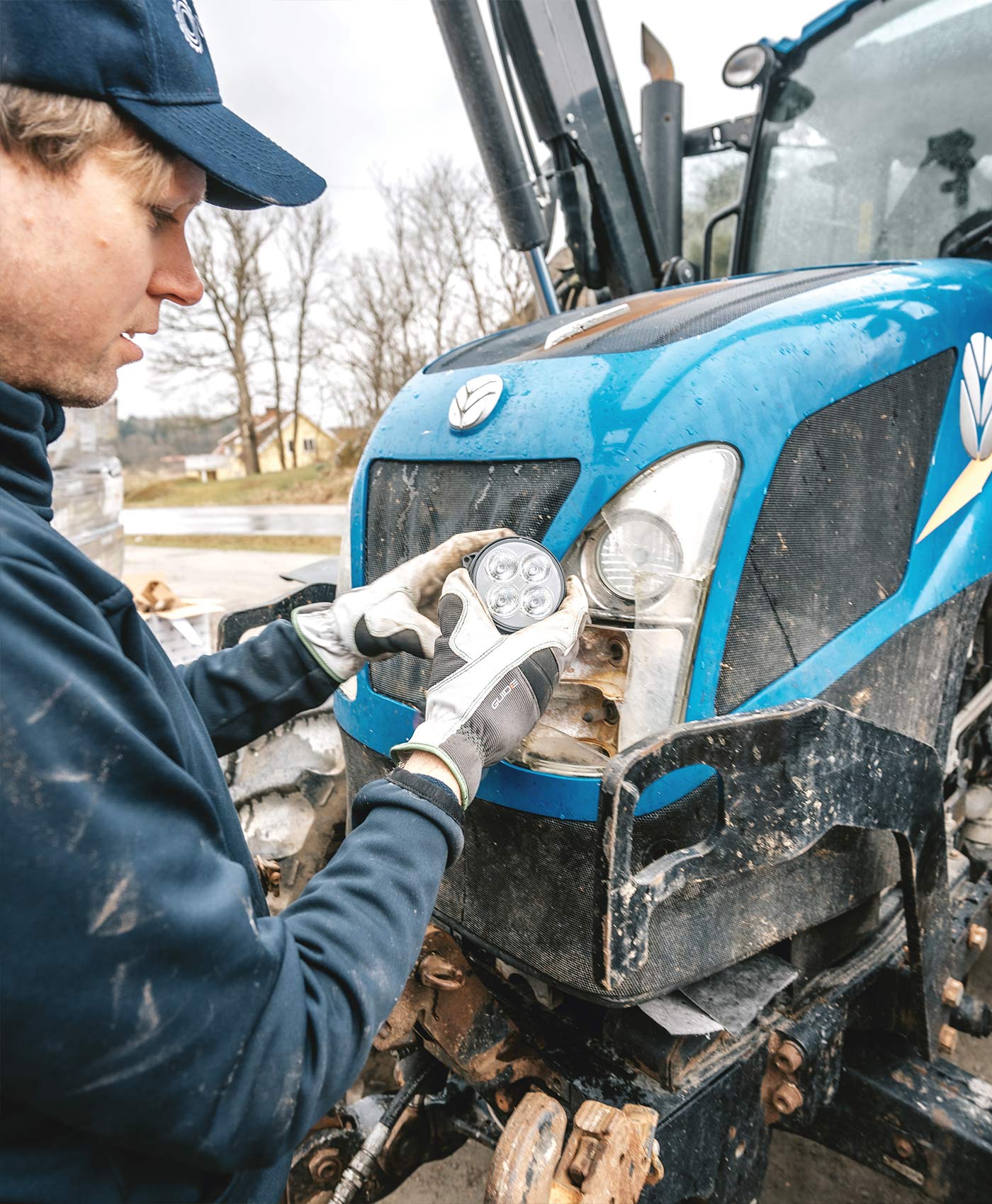 A person is installing vehicle lighting on a New Holland tractor.