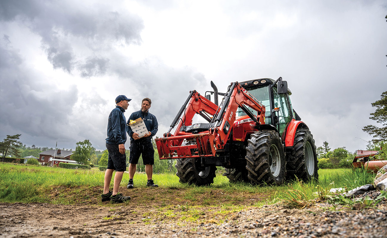 Two people are standing next to a Massey Ferguson tractor. One person is holding a box from Olsson Parts.